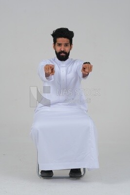 close-up of a Saudi man in traditional Saudi dress, sitting on a chair pointing , Saudi model, white background