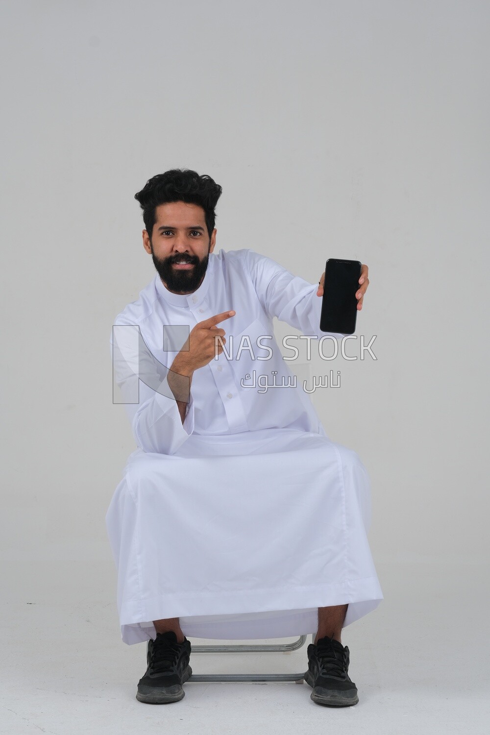 Saudi man using a mobile phone pointing on it, communicating with individuals, online requests and marketing, social relations, using technical devices, white background