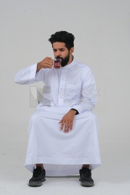 رجل سعودي يرتدي ثوبًا أبيض ، يحتسى كوبًا من الشاي ، ثقة بالنفس ، خلفية بيضاء ، موديل سعودي