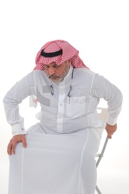 elderly Saudi man trying to sit on a chair, back and spine pain, fatigue and exhaustion, muscle spasms, health problems, white background, Saudi model