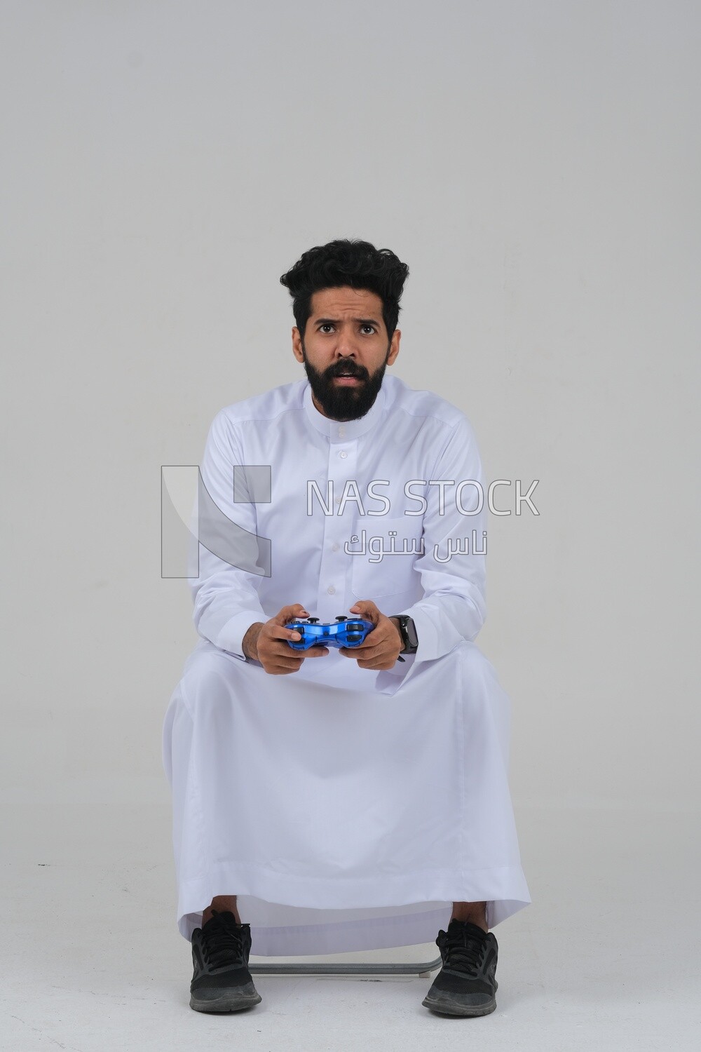 رجل سعودي يمسك بيده عصا تحكم ، يلعب ألعاب الفيديو ، بحركات وتعبيرات تدل على التركيز والانسجام ، المرح والترفيه ، بألعاب الفيديو ، ألعاب بلاي ستيشن الترفيهية ، تقنياتها وألعابها