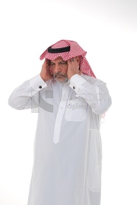 رجل سعودي مسن يديه على رأسه ، يشعر بالألم والصداع ، يرتدي ثوبا أبيض مع شماغ وعقال ، خلفية بيضاء ، رجل مسن يعاني من ألم في رأسه ، مفهوم لغة الجسد وتعبيرات الوجه.
