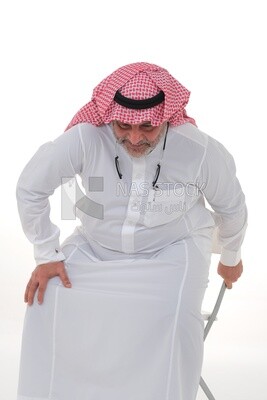 elderly Saudi man trying to sit on a chair, back and spine pain, fatigue and exhaustion, muscle spasms, health problems, white background, Saudi model