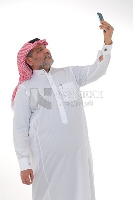 رجل سعودي  يستخدم هاتف محمول ، يلتقط صورة شخصية ، يتواصل مع الأفراد ، طلبات وتسويق عبر الإنترنت ، علاقات اجتماعية ، باستخدام أجهزة تقنية ، خلفية بيضاء