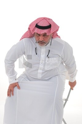 elderly Saudi man trying to sit on a chair, back and spine pain, fatigue and exhaustion, muscle spasms, health problems, white background, Saudi model