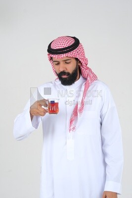 رجل سعودي يرتدي ثوبًا أبيض ، يحتسى كوبًا من الشاي ، ثقة بالنفس ، خلفية بيضاء ، موديل سعودي