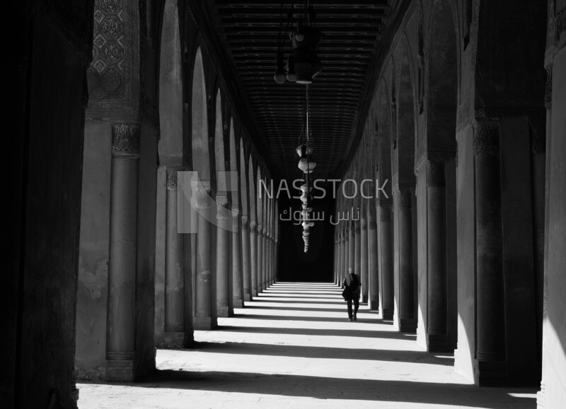 Man wanders inside the Ibn Tulun Mosque and the shadows around the columns create a beautiful atmosphere