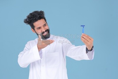 رجل سعودي يحمل شفرة حلاقة ، يزيل شعر الوجه ، العناية بالبشرة والنظافة ، يحلق لحيته ، العناية الذاتية ، موديل سعودى ، خلفية بيضاء