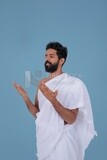 Side of a Saudi man wearing the Ihram dress and raising his hands to supplicate to God, Islam and worship, performing Hajj and Umrah, remembrances and supplications, white background, Saudi model