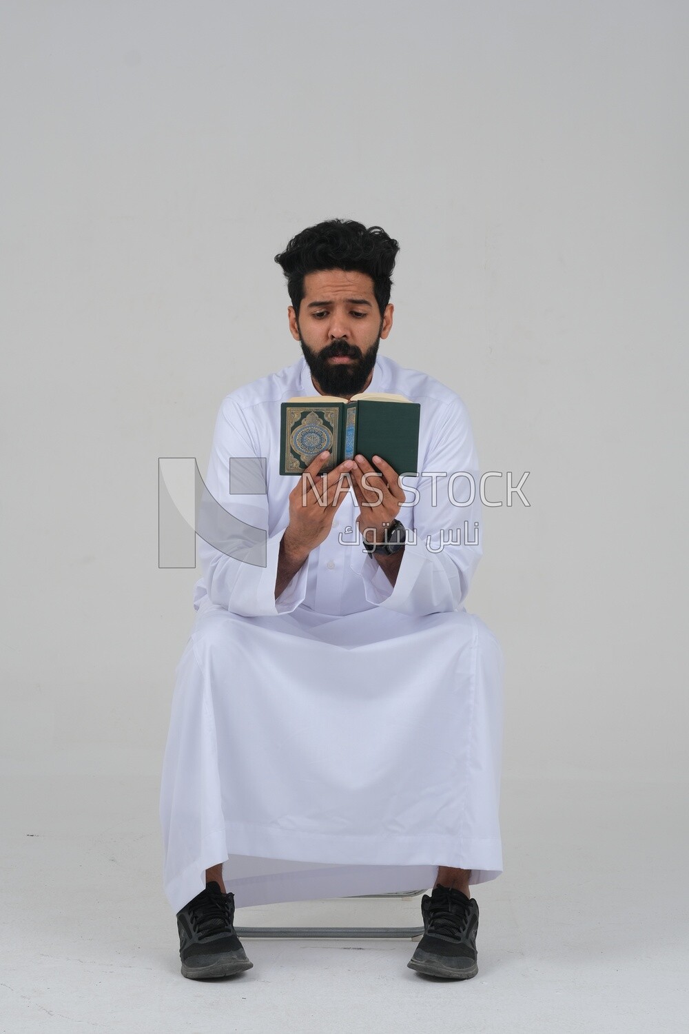 Saudi man wearing a white dress sitting on a chair, reading Quran, Islam and worship, Saudi model, white background