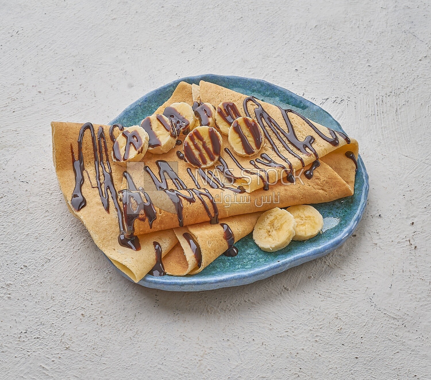 Chocolate crepe with banana slices on a solid background