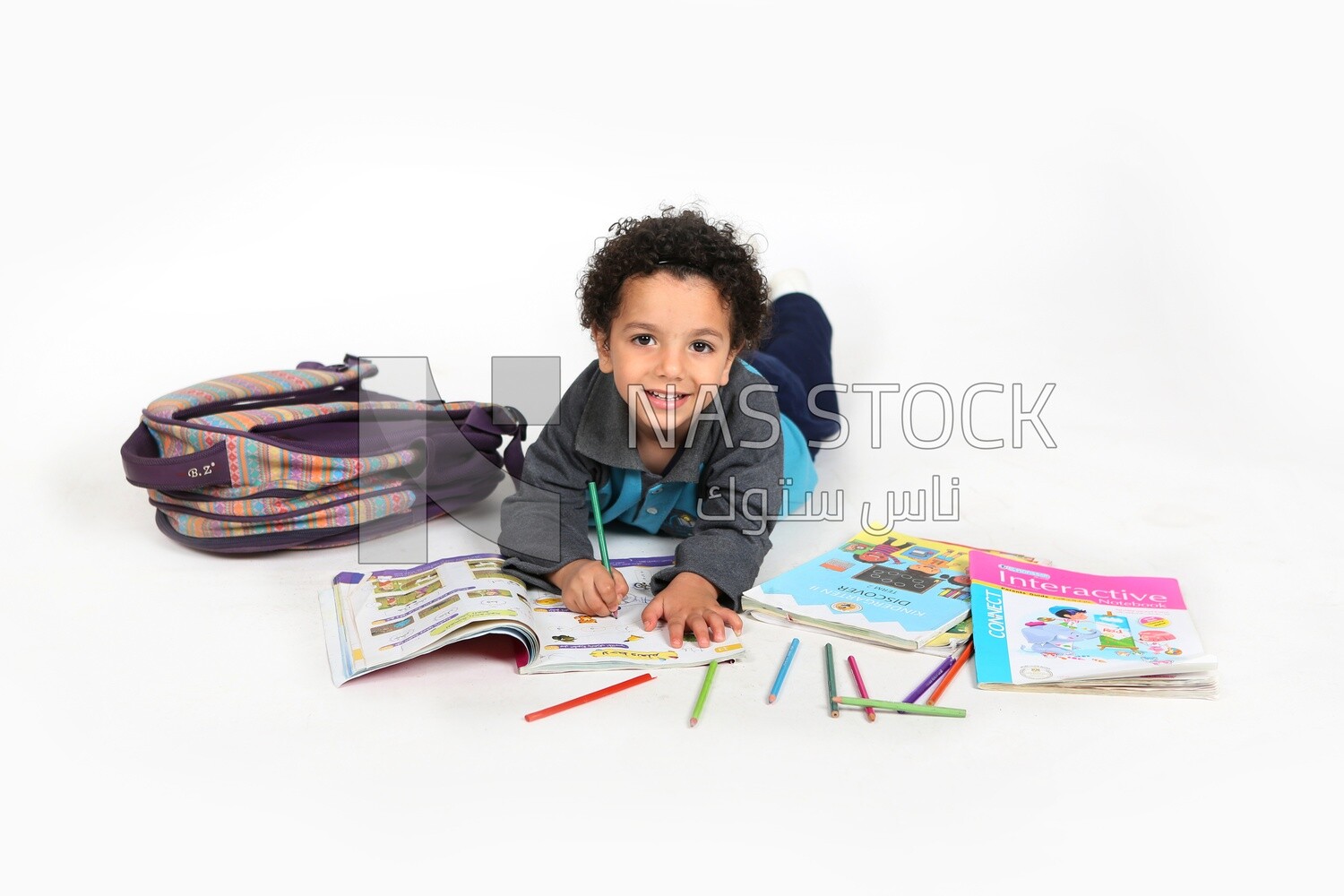 A schoolboy sitting on the floor beside his bag