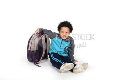 A schoolboy sitting on the floor beside his bag