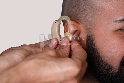 Doctor&#39;s Hand Inserting Hearing Aid In Male Patient&#39;s Ear