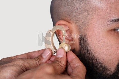 Doctor&#39;s Hand Inserting Hearing Aid In Male Patient&#39;s Ear