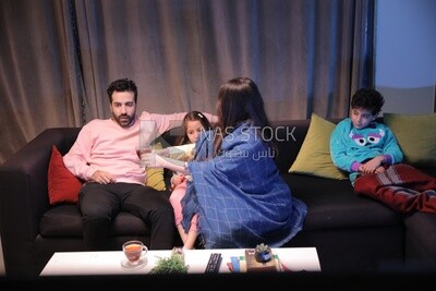 عائلة مكونة من اربعة يشاهدون التلفزيون والام تعطى الاب كوب من الشاى