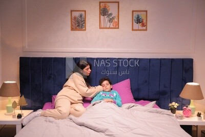 a woman sitting in bed takes her son&#39;s temperature