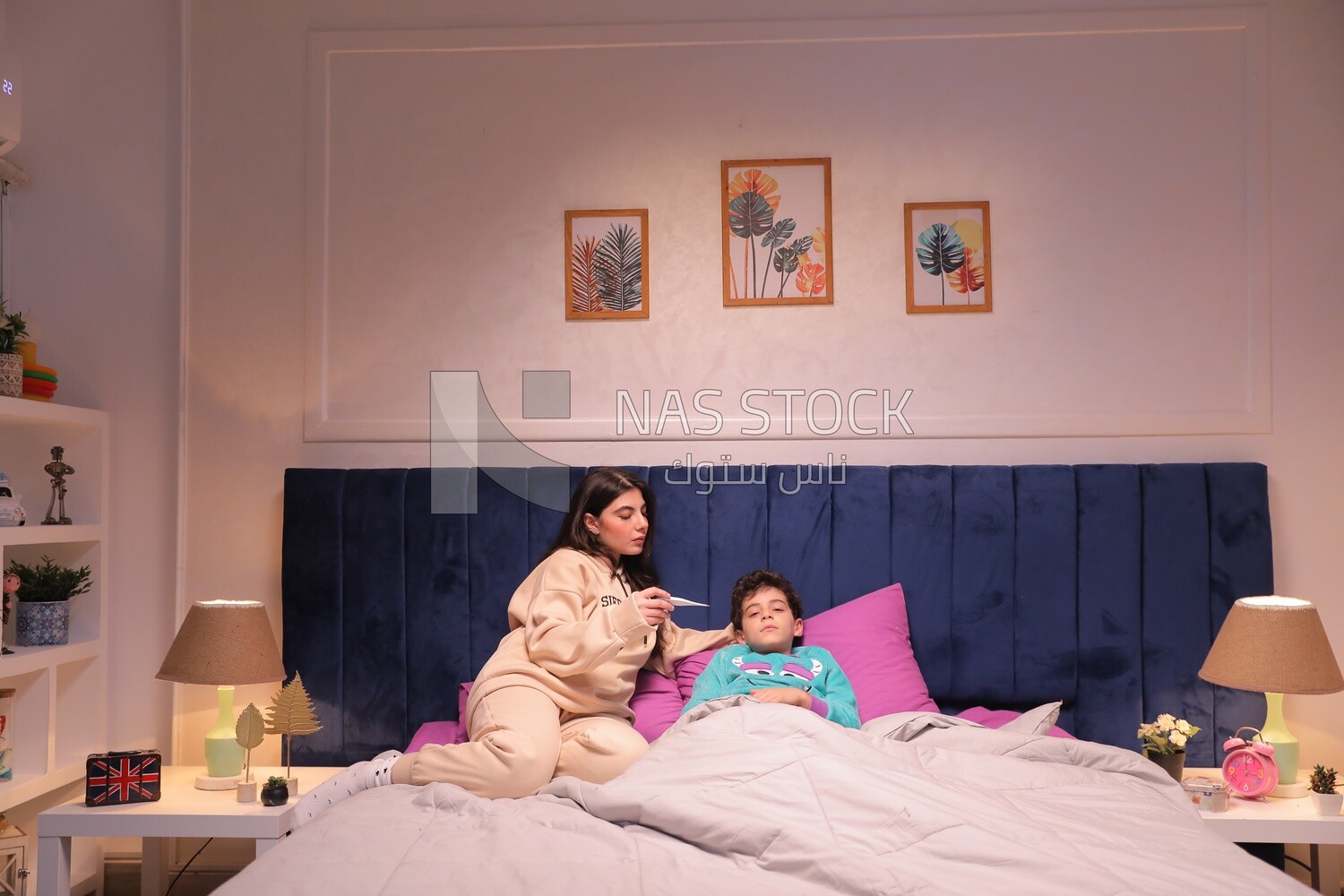 a woman sitting in bed takes her son&#39;s temperature
