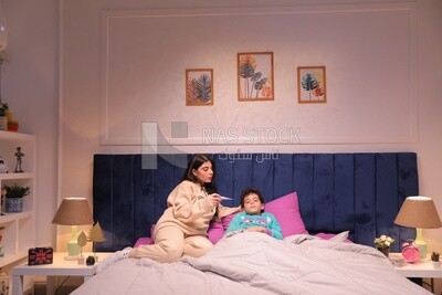 a woman sitting in bed takes her son&#39;s temperature