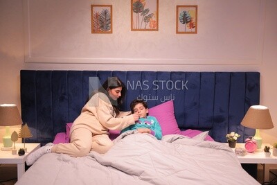 a woman sitting in bed takes her son&#39;s temperature