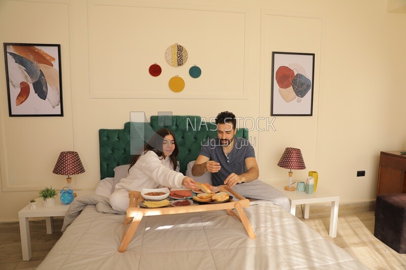 a man and a woman having breakfast on the bed