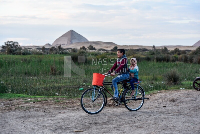Boy rides a bike and his sister sits behind him