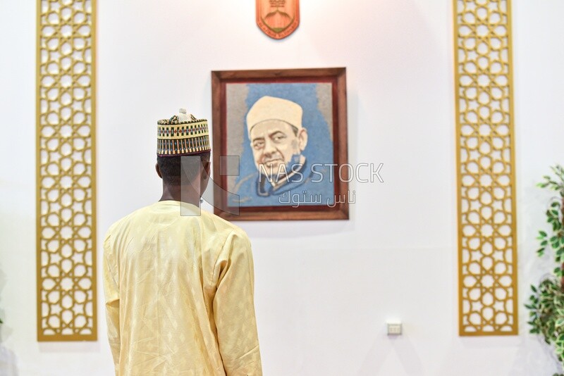 A scene of a person watching a Portrait for Sheikh of Al-Azhar hanging in the book exhibition