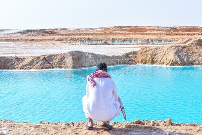 A man sits on the beach of one of the salt lakes in Siwa