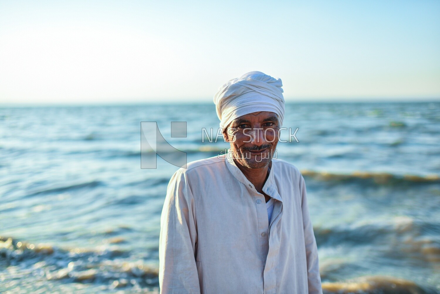 A scene of an Egyptian man standing smiling on the seashore