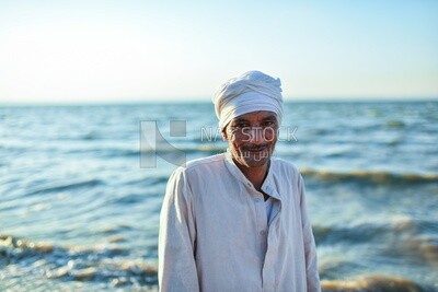 A scene of an Egyptian man standing smiling on the seashore