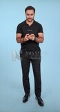 Photo Of a Handsome man Standing and holding his mobile, Smiling Man, Wearing Casual Clothes Posing In a Light Room Interior, Smiling At the Camera