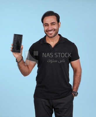 Photo Of a Handsome man Standing and holding his mobile, Smiling Man, Wearing Casual Clothes Posing In a Light Room Interior, Smiling At the Camera