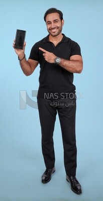 Photo Of a Handsome man Standing and holding his mobile pointing on it, Smiling Man, Wearing Casual Clothes Posing In a Light Room Interior, Smiling At the Camera