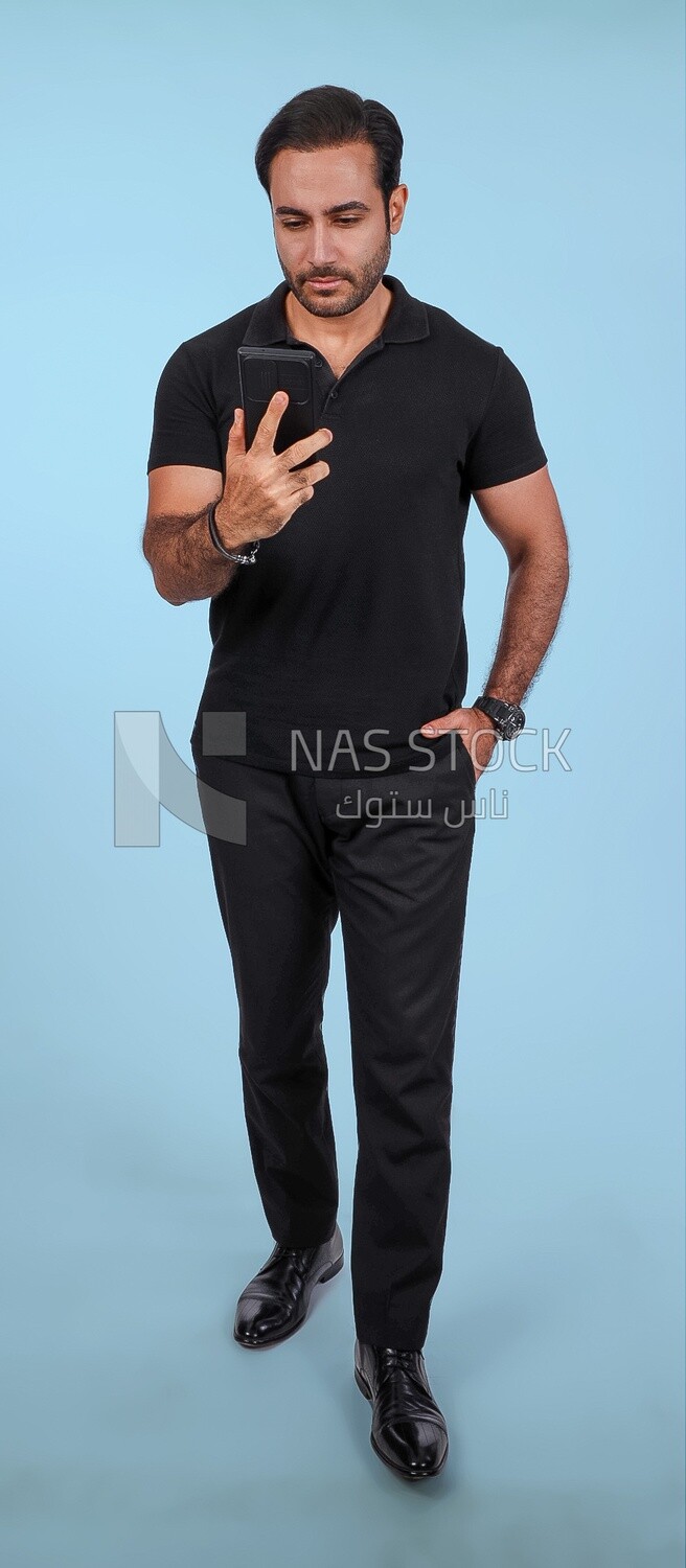 Photo Of a Handsome man Standing and holding his mobile, Smiling Man, Wearing Casual Clothes Posing In a Light Room Interior, Smiling At the Camera