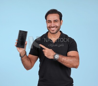 Photo Of a Handsome man Standing and holding his mobile, Smiling Man, Wearing Casual Clothes Posing In a Light Room Interior, Smiling At the Camera