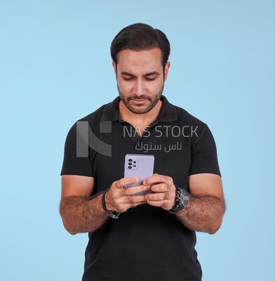 Photo Of a Handsome man Standing and holding his mobile, Smiling Man, Wearing Casual Clothes Posing In a Light Room Interior, Smiling At the Camera