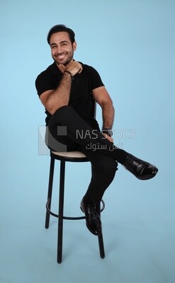Photo of a Handsome man sitting on a chair and putting a leg on a leg, Smiling Man, Wearing Casual Clothes Posing In a Light Room Interior, Smiling At the Camera