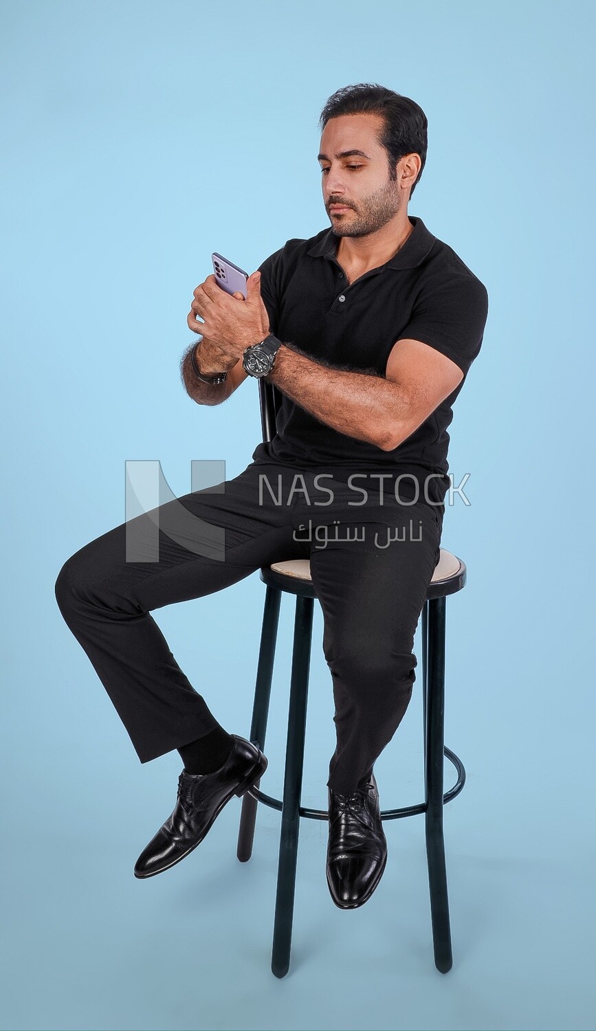 Photo Of a Handsome man sitting on the chair and holding his mobile, Smiling Man, Wearing Casual Clothes Posing In a Light Room Interior, Smiling At the Camera