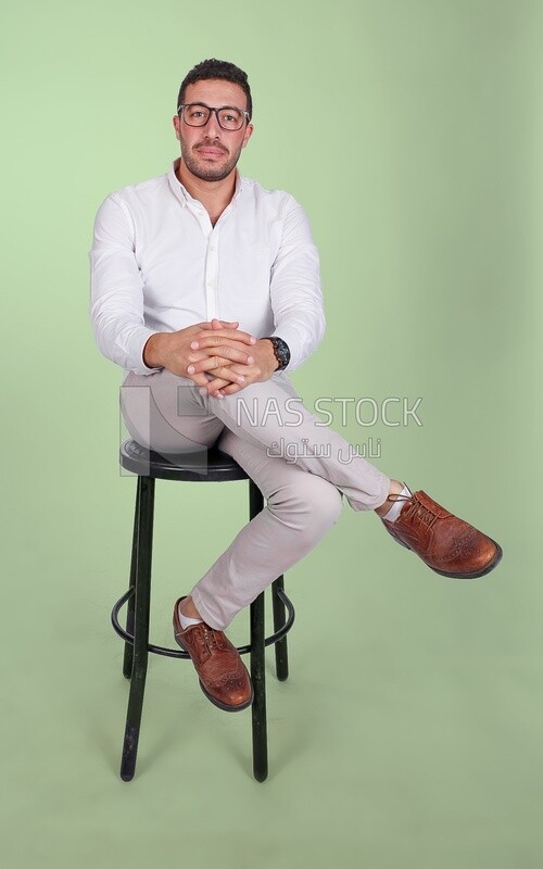 Photo of a Handsome man sitting on a chair and putting a leg on a leg, Smiling Man, Wearing formal Clothes Posing In a Light Room Interior, Smiling At the Camera