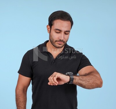 صورة لرجل وسيم يقف وينظر إلى ساعته، رجل مبتسم، يرتدي ملابس غير رسمية في غرفة خفيفة داخلية، يبتسم للكاميرا