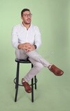 Photo of a Handsome man sitting on a chair and putting a leg on a leg, Smiling Man, Wearing formal Clothes Posing In a Light Room Interior, Smiling At the Camera