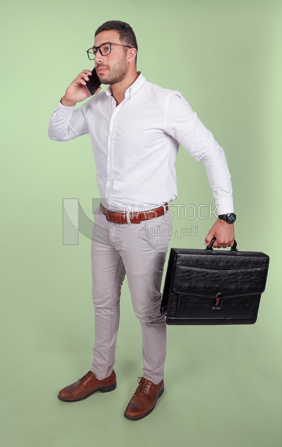 Photo of a handsome man wearing glasses talking on his phone and holding a leather bag, business and partnership development, business meeting, model