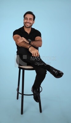 Photo of a Handsome man sitting on a chair and putting a leg on a leg, Smiling Man, Wearing Casual Clothes Posing In a Light Room Interior, Smiling At the Camera