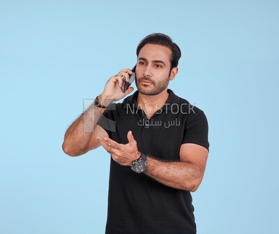 Portrait of a handsome man standing and talking to the mobile phone looking annoyed, man smiling, dressed in casual clothes in light room interior, smiling at camera