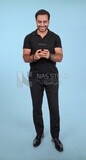 Photo Of a Handsome man Standing and holding his mobile, Smiling Man, Wearing Casual Clothes Posing In a Light Room Interior, Smiling At the Camera