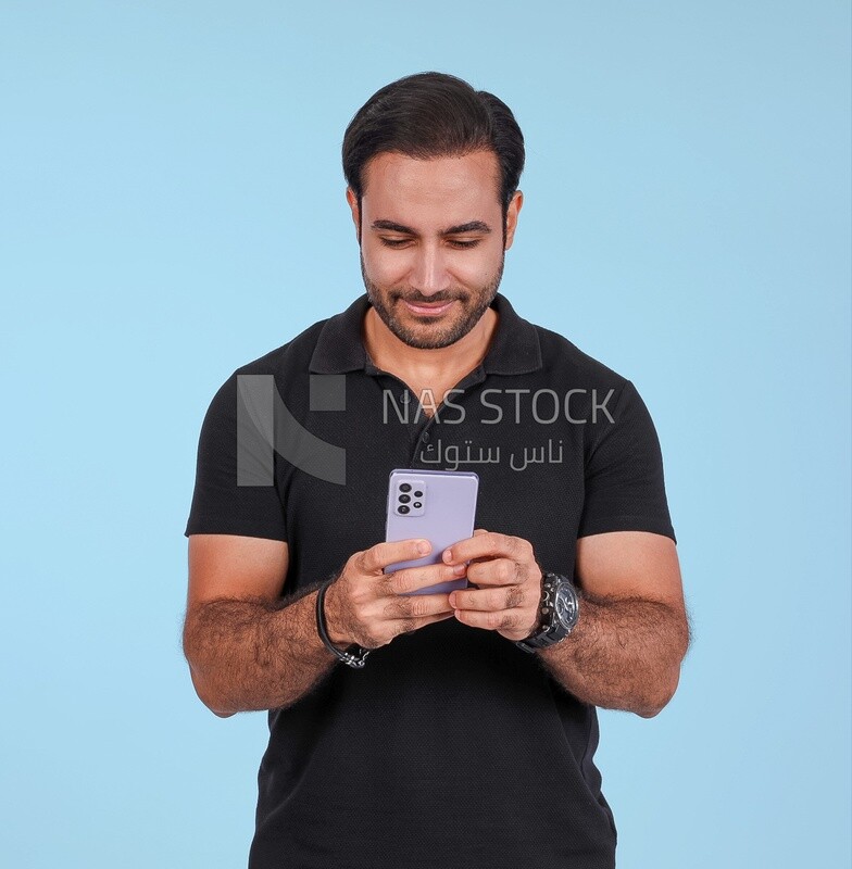 Photo Of a Handsome man Standing and holding his mobile, Smiling Man, Wearing Casual Clothes Posing In a Light Room Interior, Smiling At the Camera