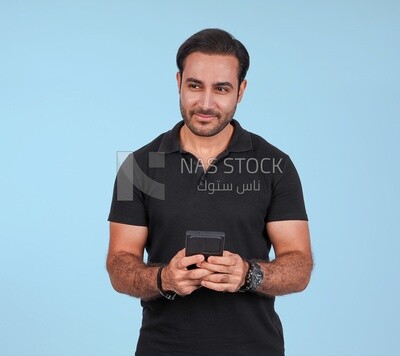 Photo Of a Handsome man Standing and holding his mobile, Smiling Man, Wearing Casual Clothes Posing In a Light Room Interior, Smiling At the Camera