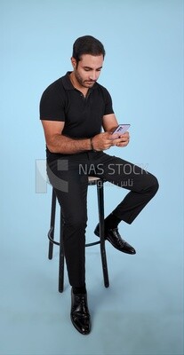 Photo Of a Handsome man sitting on the chair and holding his mobile, Smiling Man, Wearing Casual Clothes Posing In a Light Room Interior, Smiling At the Camera