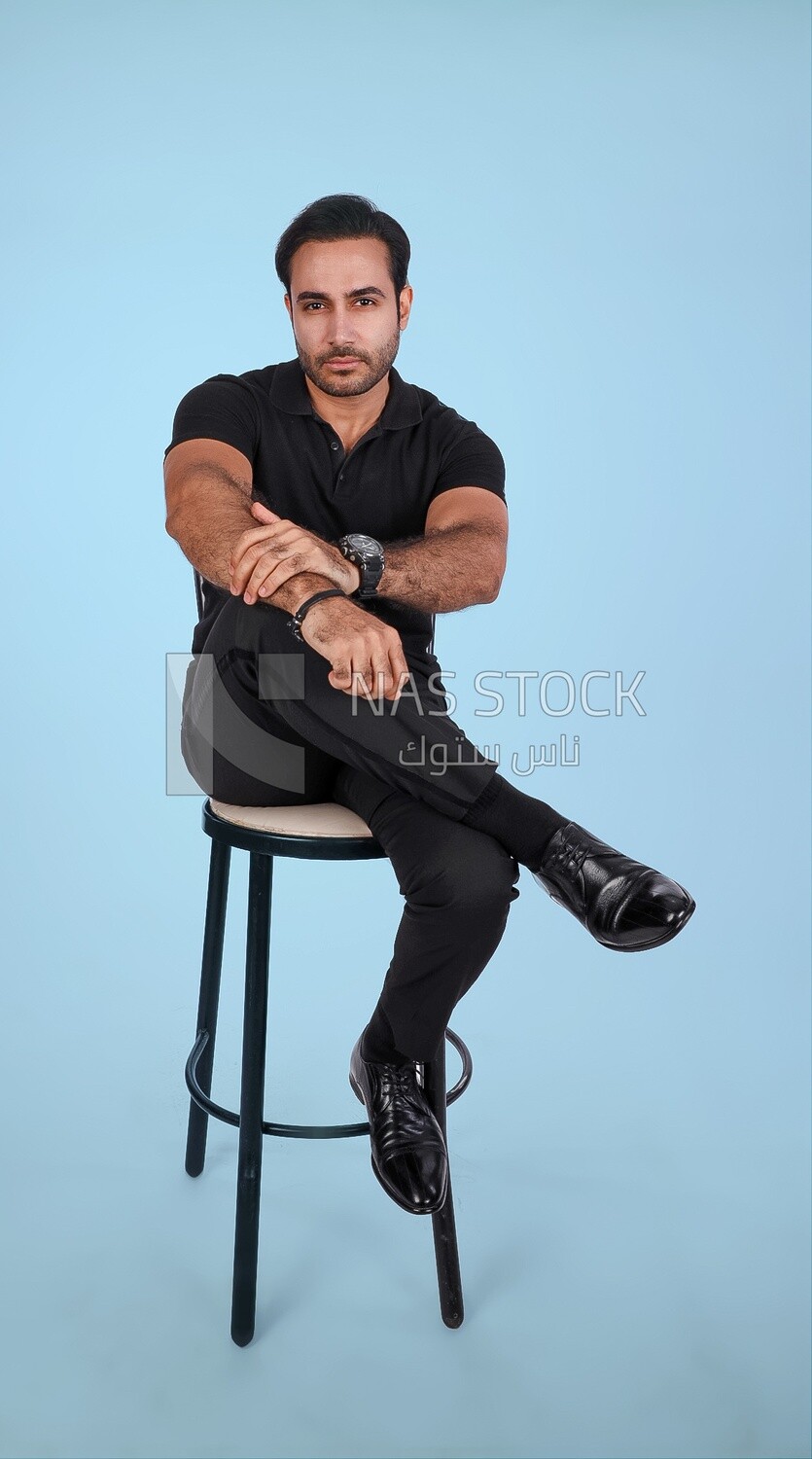 Photo Of a Handsome man sitting on the chair and puts a leg on a leg , Smiling Man, Wearing Casual Clothes Posing In a Light Room Interior, Smiling At the Camera