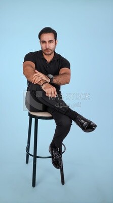 Photo Of a Handsome man sitting on the chair and puts a leg on a leg , Smiling Man, Wearing Casual Clothes Posing In a Light Room Interior, Smiling At the Camera
